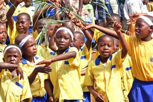 A group of waving children dressed in yellow uniforms at Linked With Love, Pearce Church's partnership with the Nzige preschool